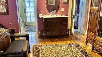 A living room with a wooden floor, a large rug, a sofa, a wooden cabinet, and a door leading to another room.