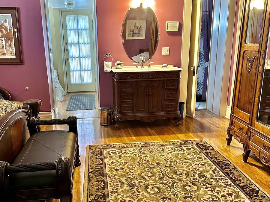 A living room with a wooden floor, a large rug, a sofa, a wooden cabinet, and a door leading to another room.