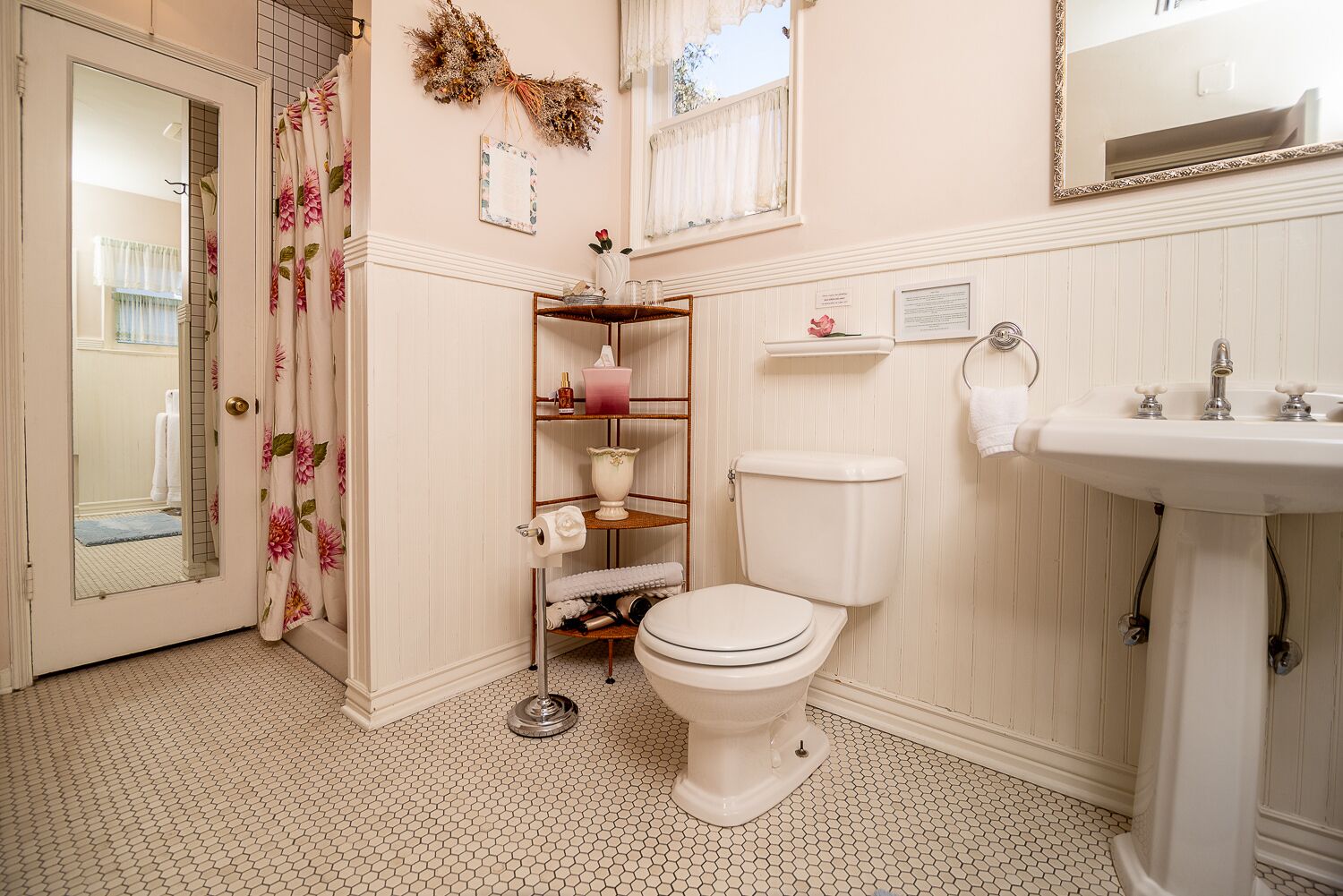 Un bagno con il water, un lavandino, una tenda da doccia con motivi floreali, uno scaffale con articoli da toilette e uno specchio.