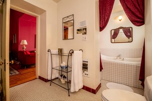 Baño con lavamanos blanco, bañera y retrete. Hay un perchero con toallas blancas y un espejo encima.