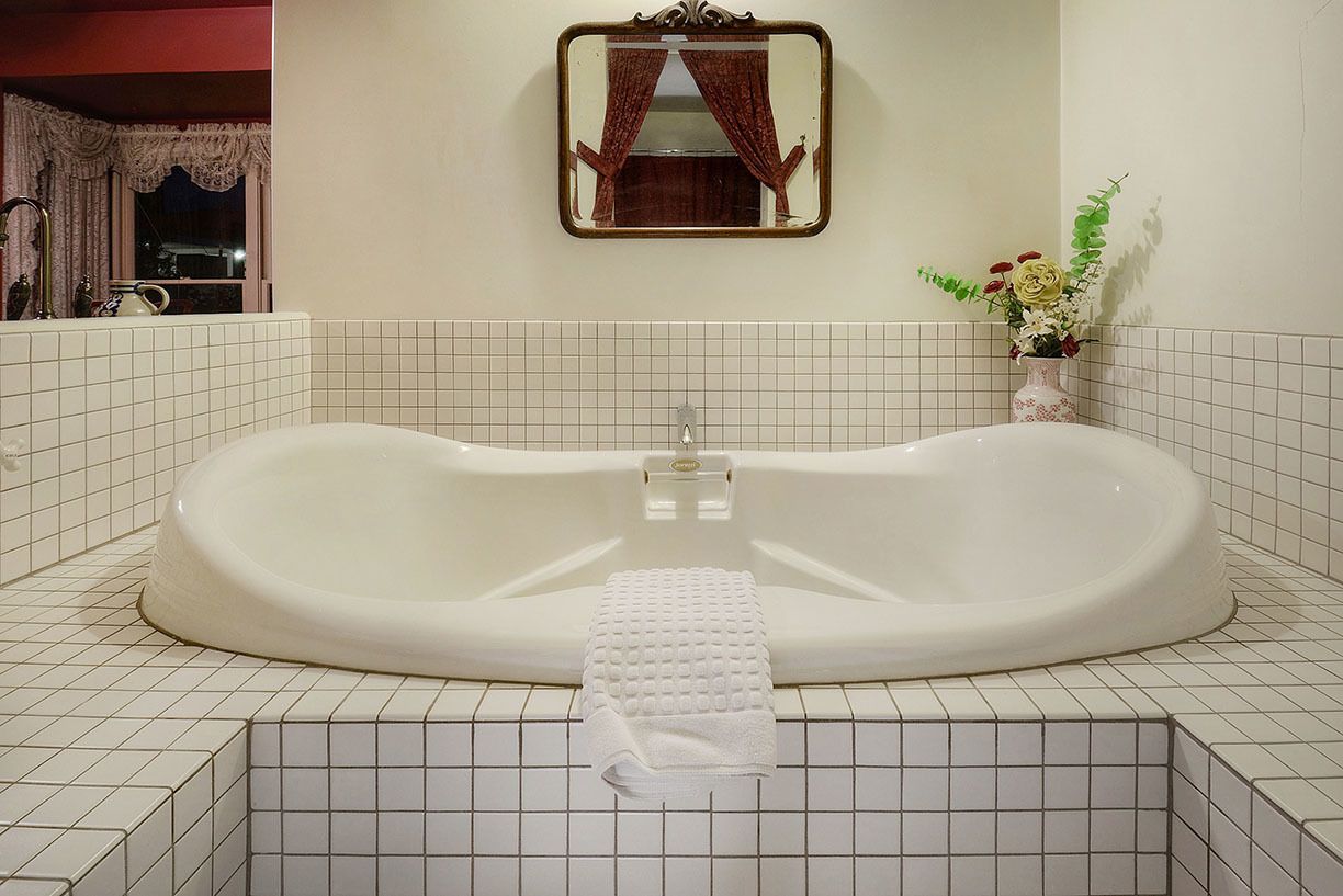 A bathroom with a large bathtub, a mirror, and a vase with flowers.