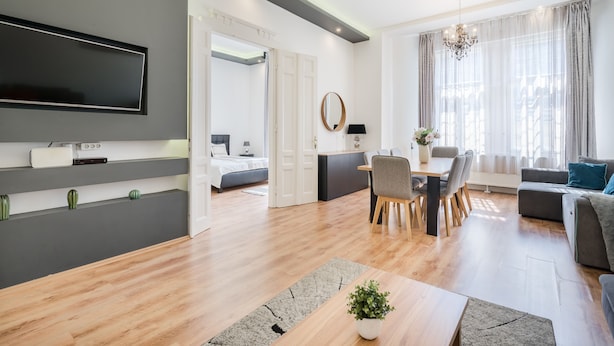 A modern living room with a flat-screen TV, a dining area with a table and chairs, a sofa, and a large window with curtains. - Real Apartments Zichy (Budapest)