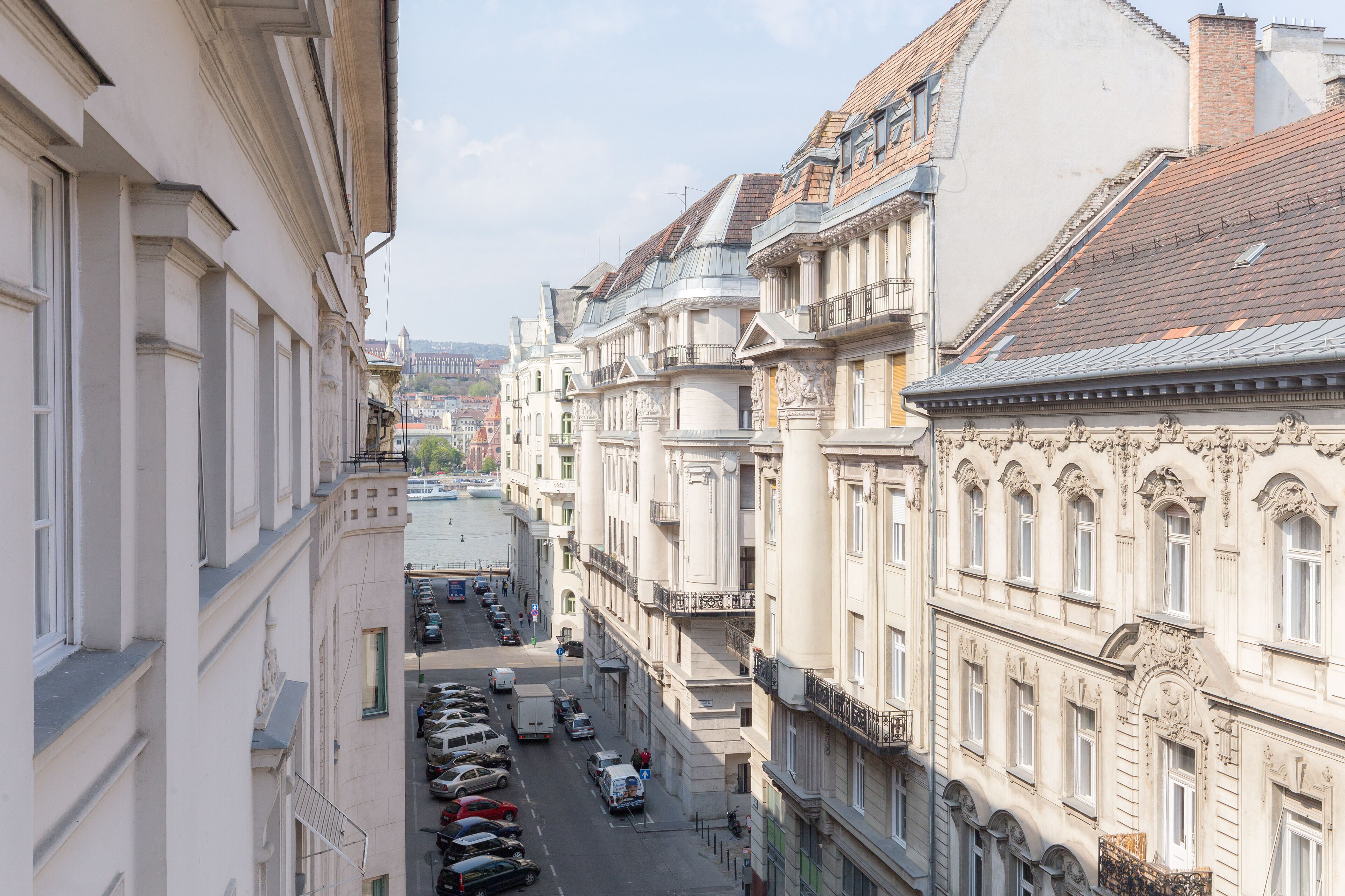 Una calle estrecha flanqueada por edificios históricos, coches aparcados y una vista despejada del paisaje urbano al fondo.