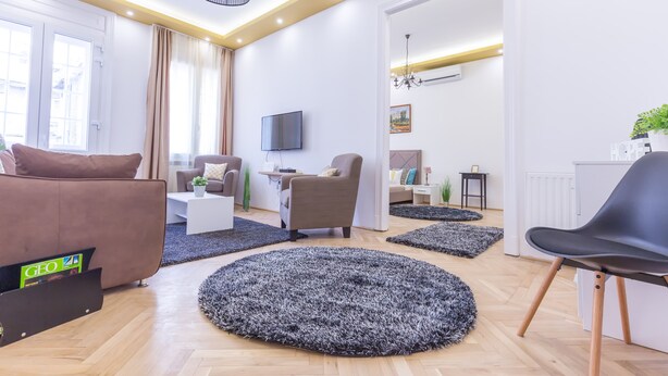 Un soggiorno moderno con divano, poltrona e tavolino. C'è una TV montata a parete e un lampadario appeso al soffitto.