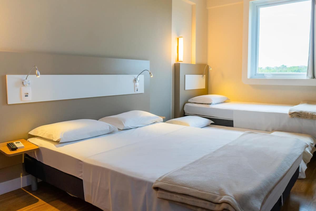 Een hotelkamer met een groot bed, een kleiner bed, een nachtkastje met een telefoon en een raam met uitzicht.