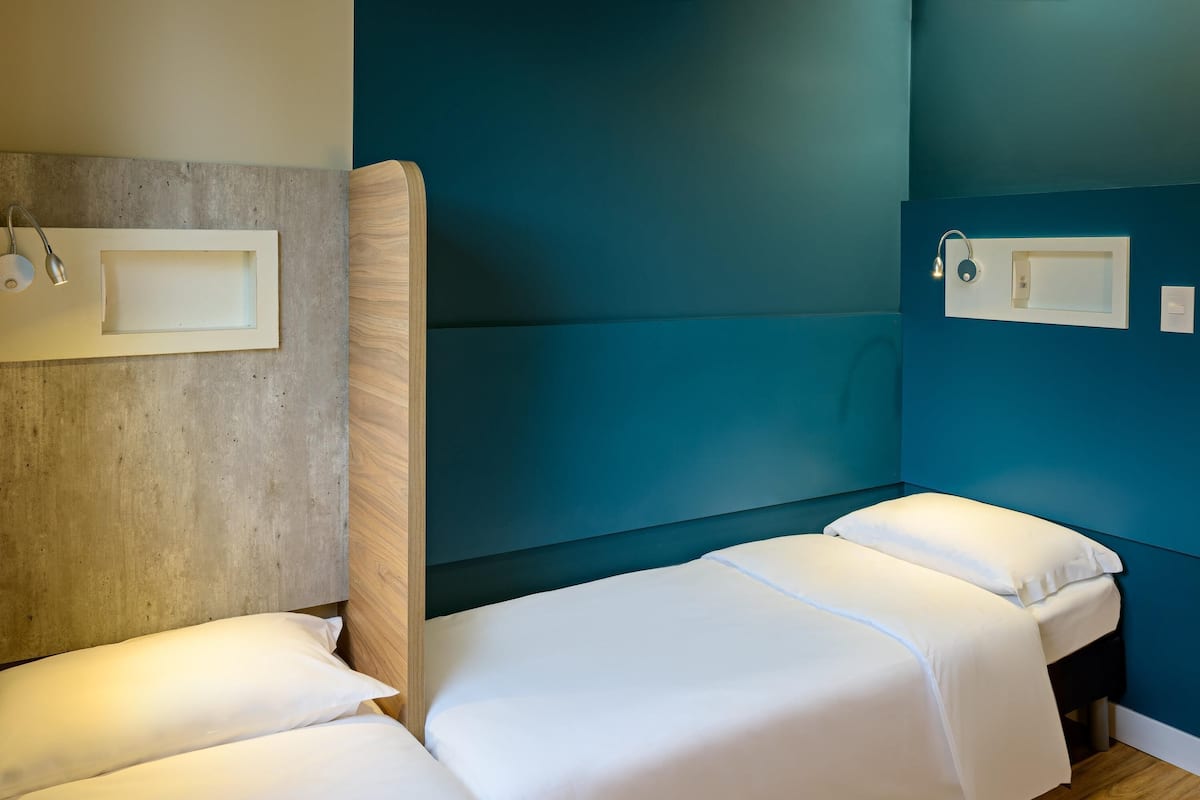 Een kamer met twee eenpersoonsbedden, een betonnen muur en wanden in een blauwgroene kleur.