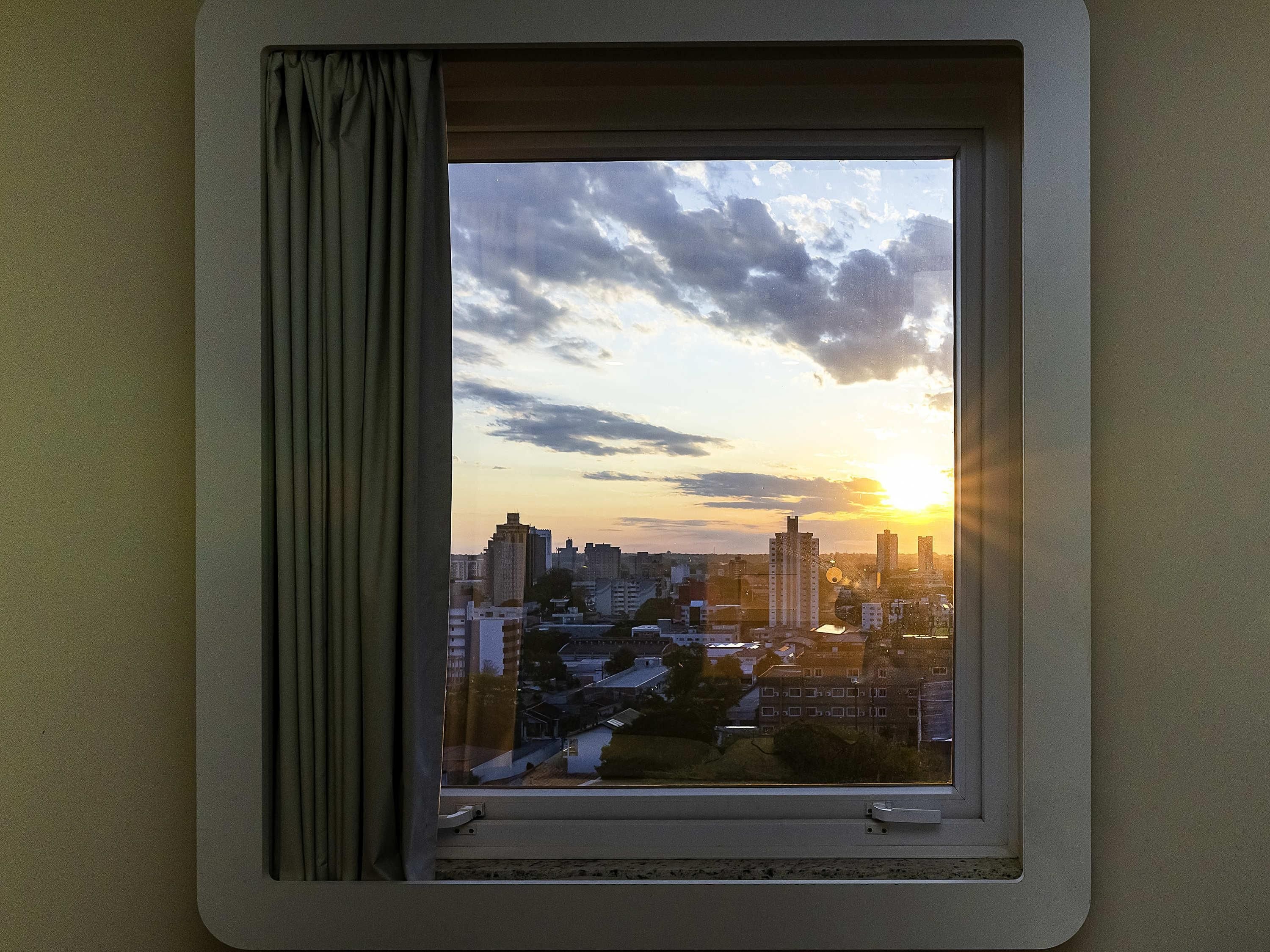 Ein Fenster mit Blick auf eine Stadtlandschaft im Abendrot.