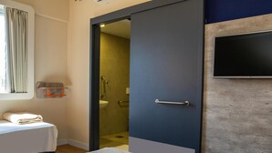 A hotel room with a bed, a bathroom with a shower, a sink, and a television on the wall. - ibis budget Foz Do Iguacu (Foz do Iguaçu)