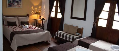 A hotel room with two beds, a wooden floor, a painting on the wall, and a window with curtains.