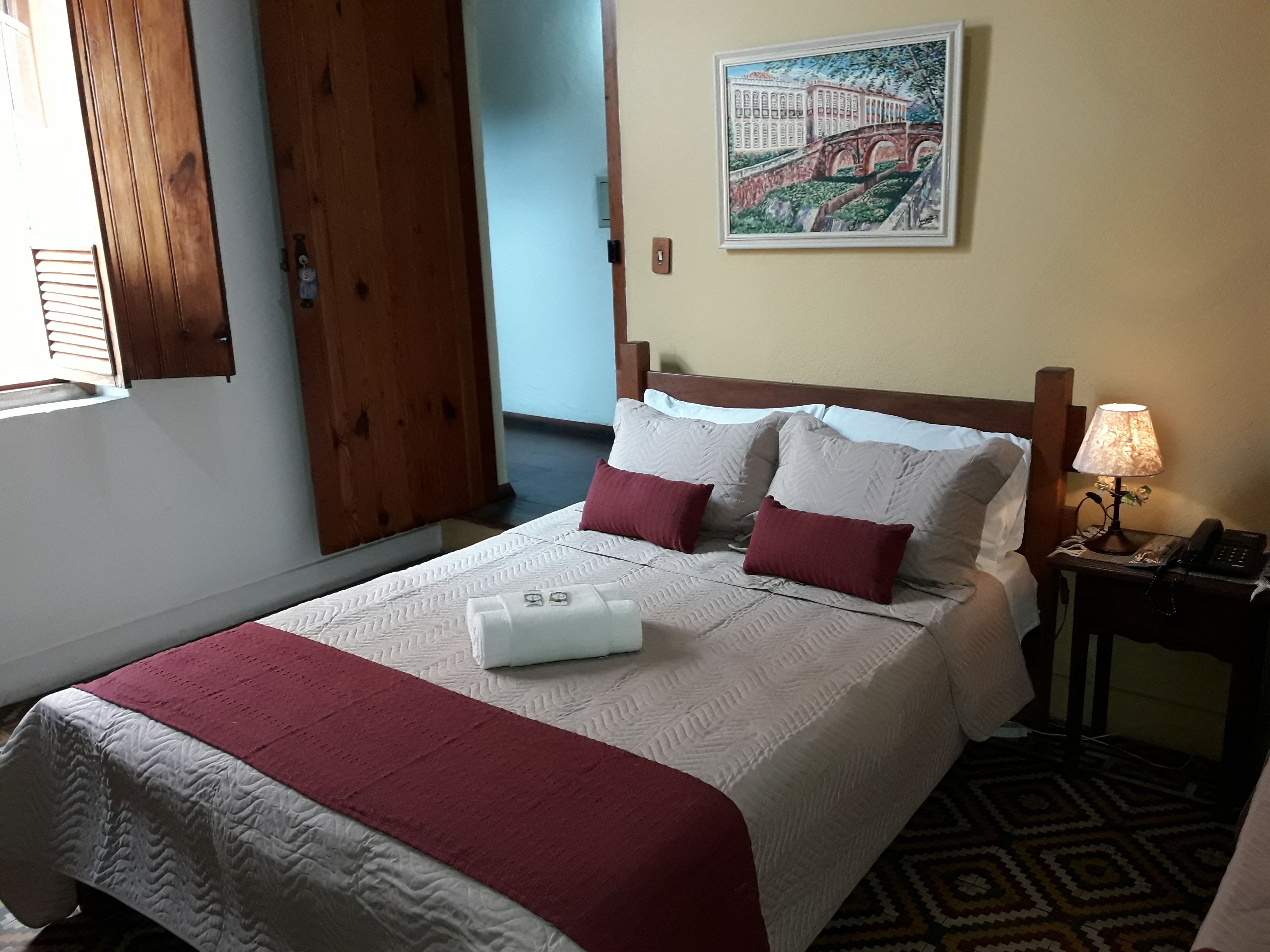 Habitación de hotel con cama, mesita de noche con lámpara, un cuadro en la pared y ventana con persianas.