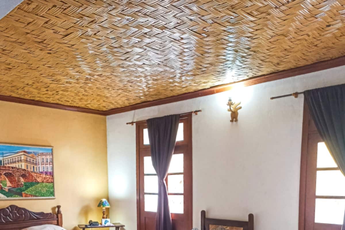 Une chambre d’hôtel avec deux lits, un plafond en bois, un tableau au mur et une fenêtre avec des rideaux.