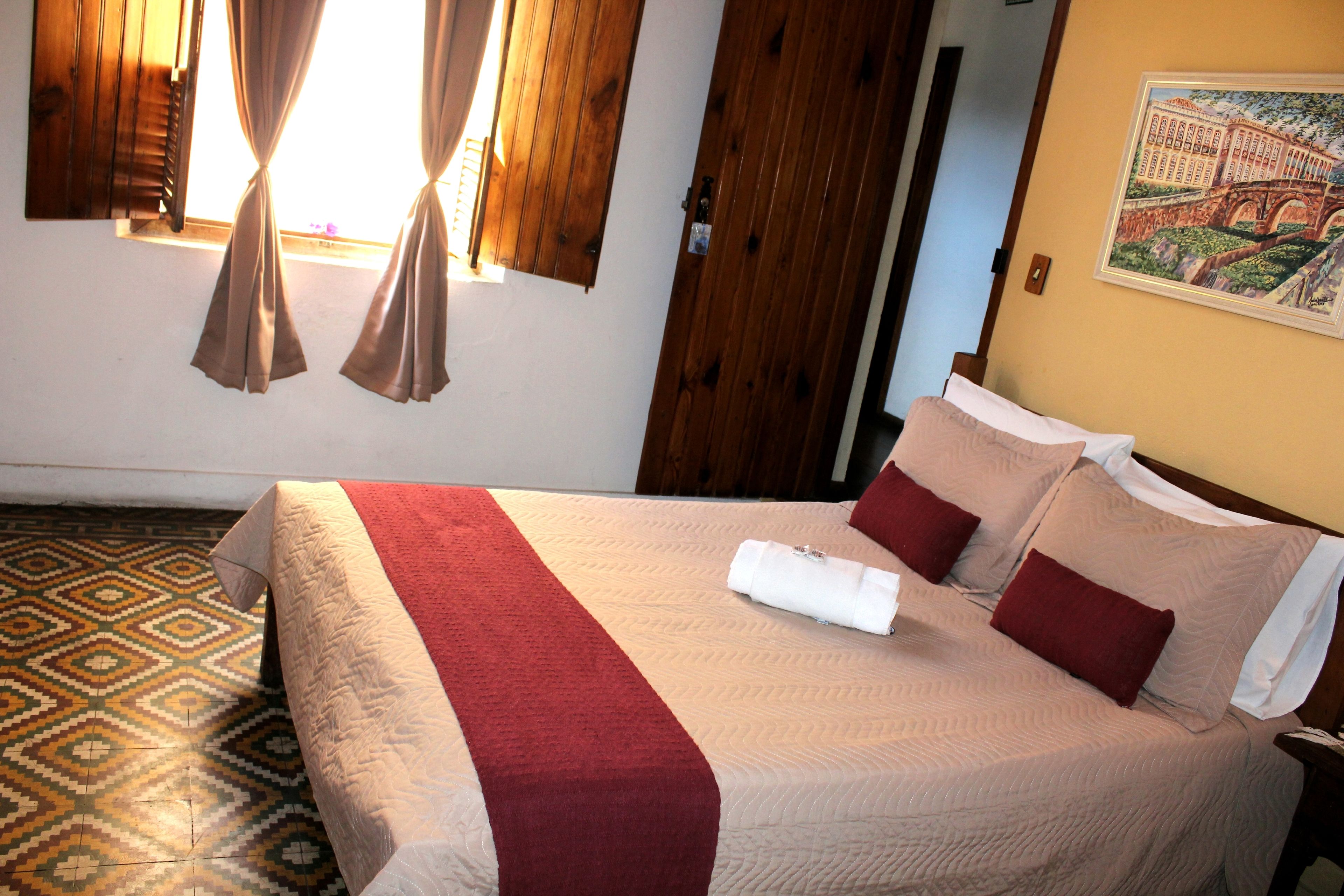 Una cama bien tendida con una colcha roja y blanca, una puerta de madera y un suelo estampado.