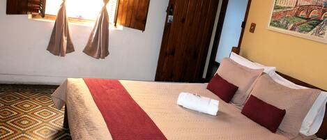 Una cama bien tendida con una colcha roja y blanca, una puerta de madera y un suelo estampado.