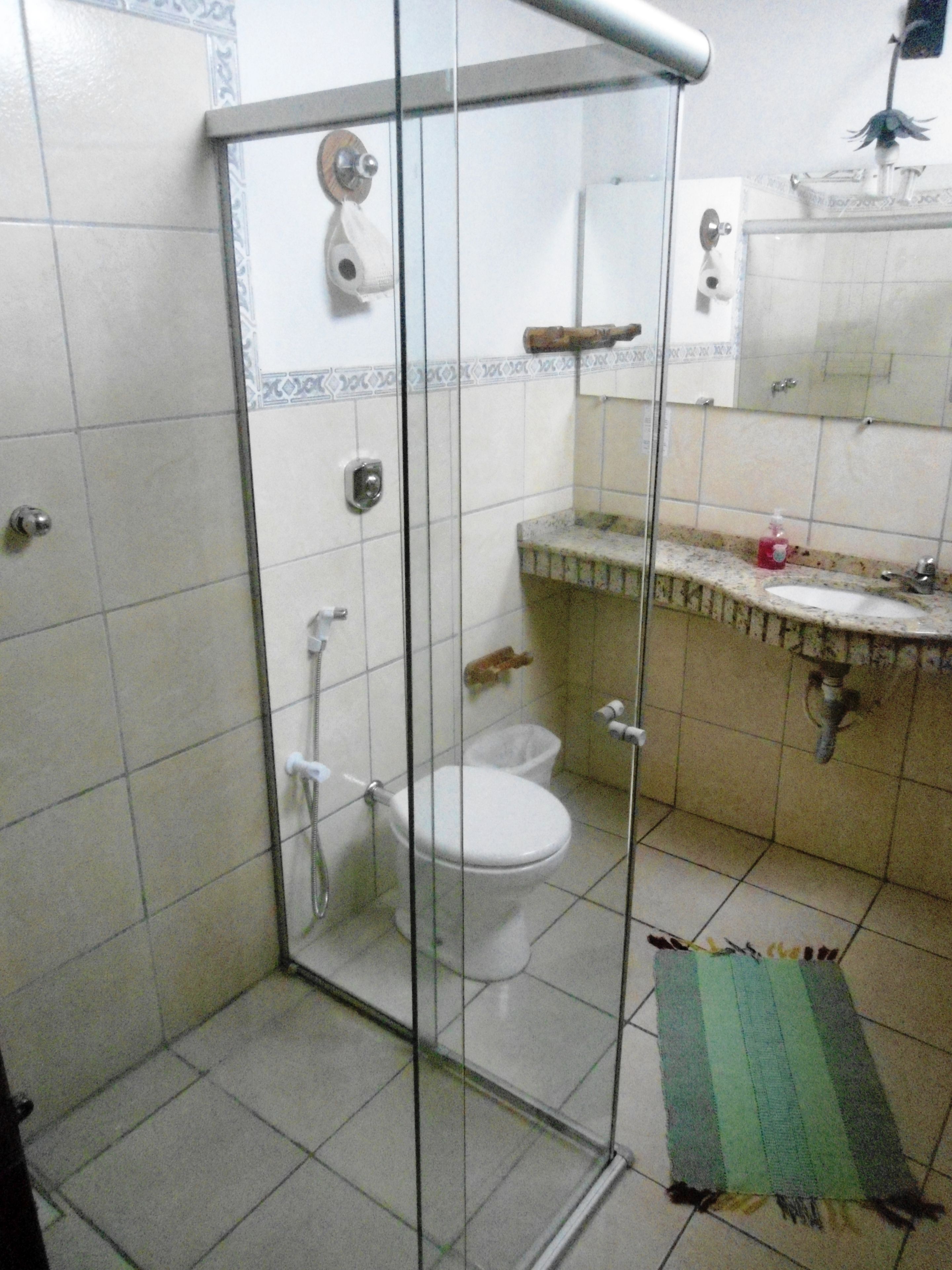 A bathroom with a glass-enclosed shower, a toilet, and a sink with a soap dispenser.