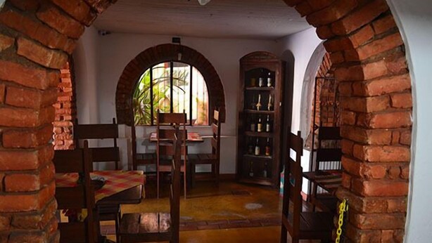 A room with brick arches, a wooden table with chairs, and a bookshelf. - Pousada Estação do Trem (São João del Rei)