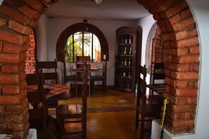 A room with brick arches, a wooden table with chairs, and a bookshelf. - Pousada Estação do Trem (São João del Rei)