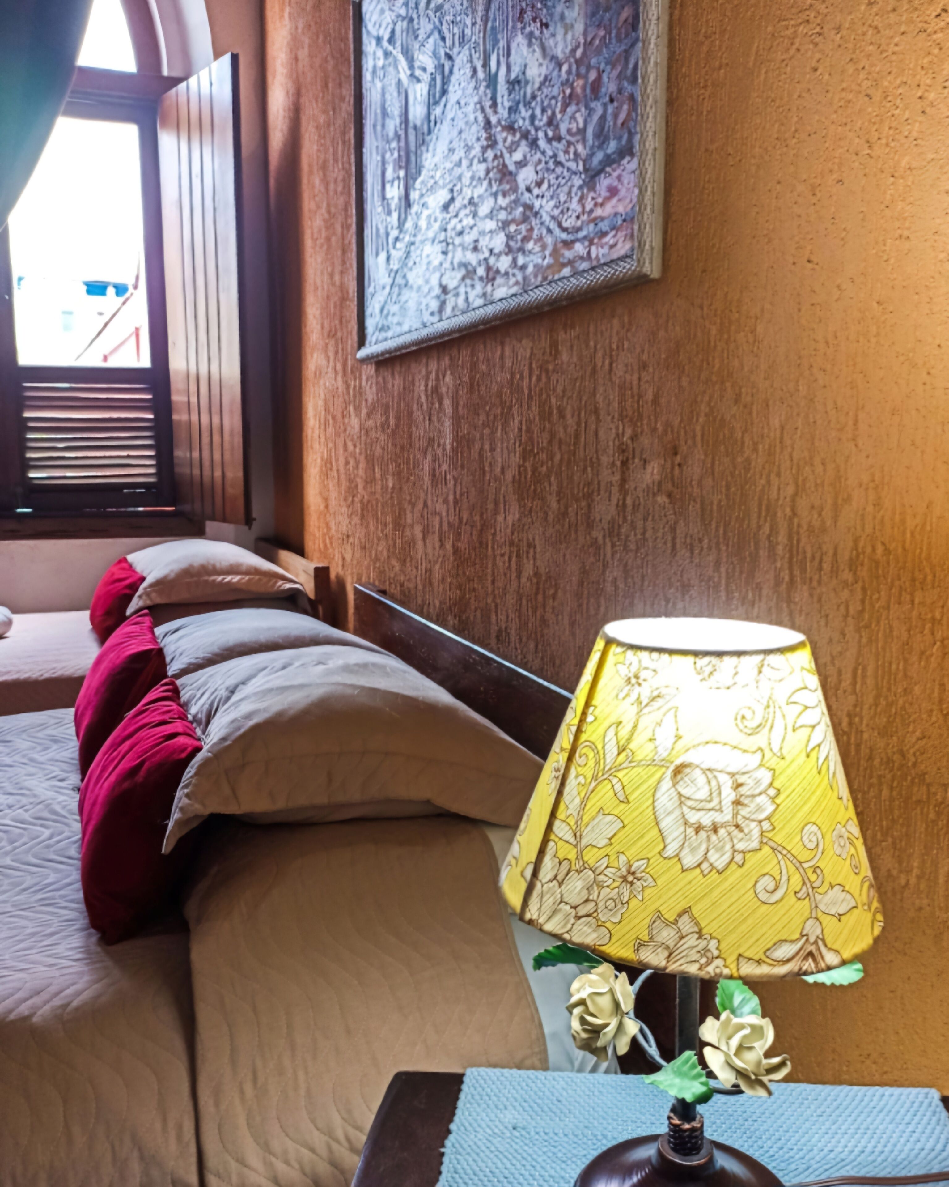 Ein Hotelzimmer mit Bett, Kissen, Lampe und einem Gemälde an der Wand.