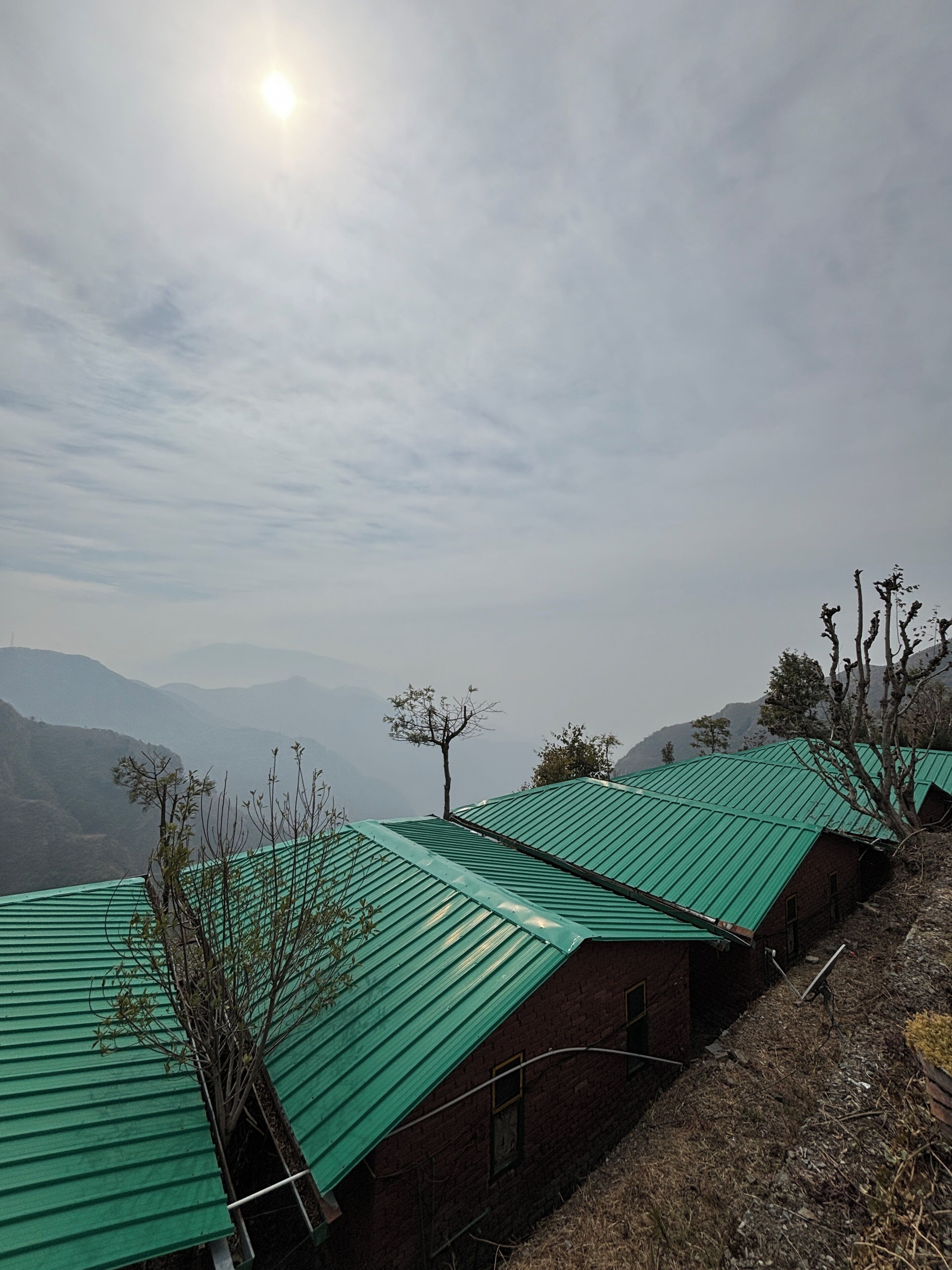 A row of brick buildings with green roofs, set against a mountainous backdrop.