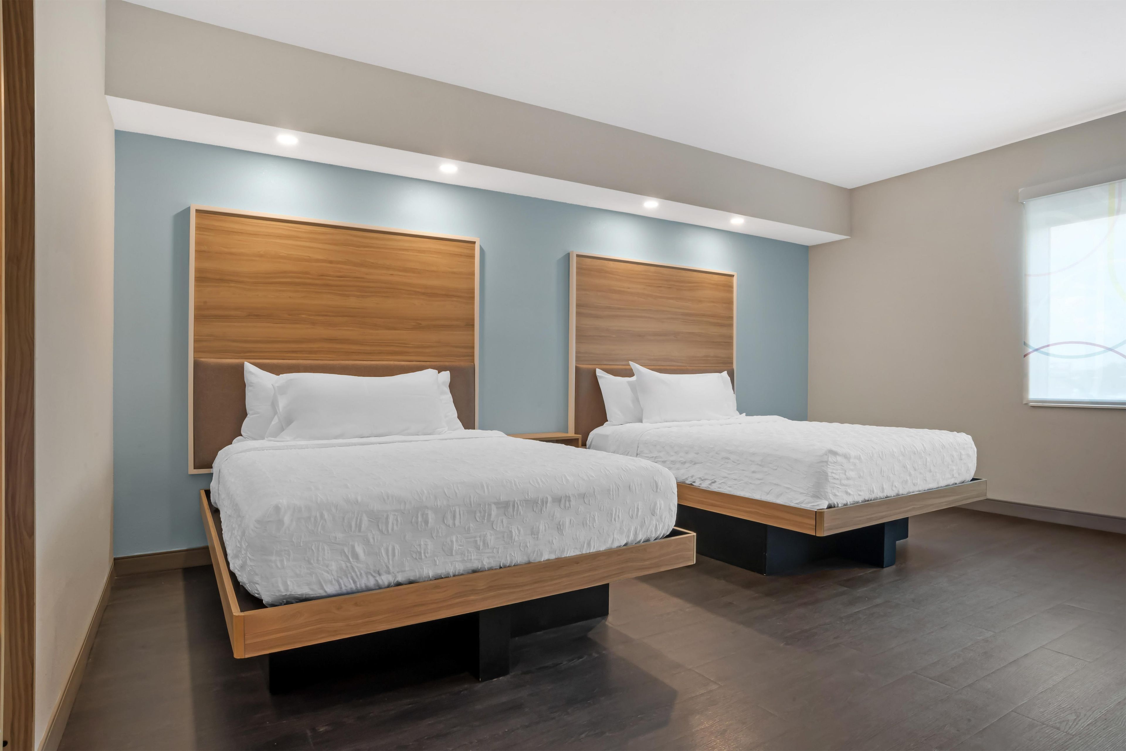 A hotel room with two beds, wooden headboards, and a large window.
