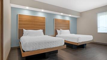 A hotel room with two beds, wooden headboards, and a large window.