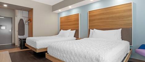 A modern hotel room with two beds, a wooden headboard, a small table, and a mirror.