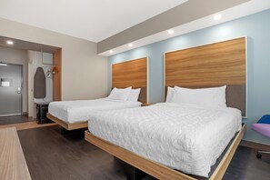 Una habitación de hotel moderna con dos camas, un cabecero de madera, una mesita pequeña y un espejo.