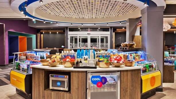Una estación de bebidas y aperitivos autoservicio con una variedad de opciones, un microondas y un refrigerador.
