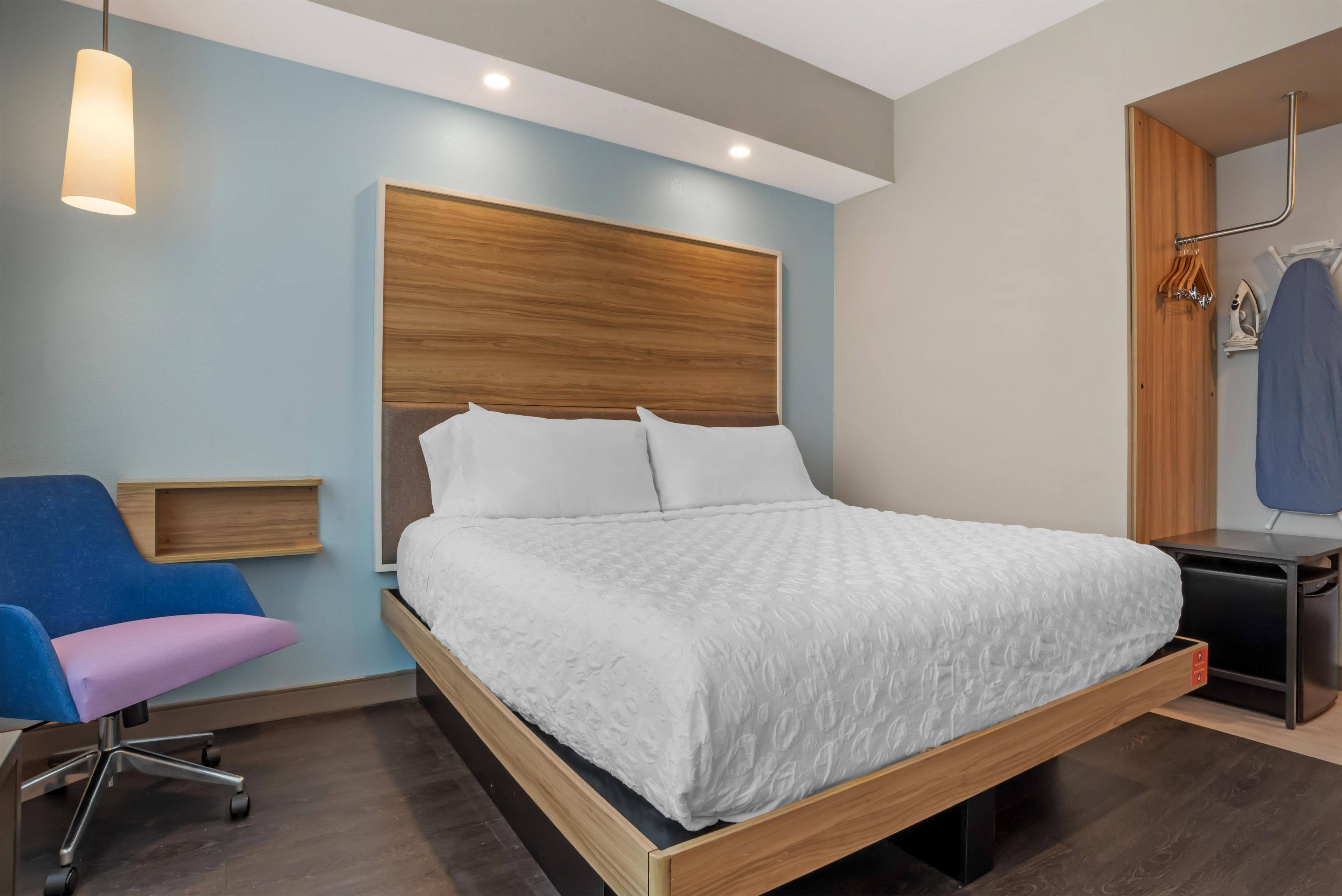 A modern bedroom with a wooden headboard, a single bed with white bedding, a desk with a chair, and a hanging clothes rack.