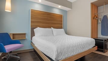 A modern bedroom with a wooden headboard, a single bed with white bedding, a desk with a chair, and a hanging clothes rack.