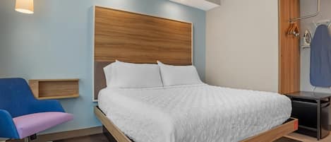 A modern bedroom with a wooden headboard, a single bed with white bedding, a desk with a chair, and a hanging clothes rack.