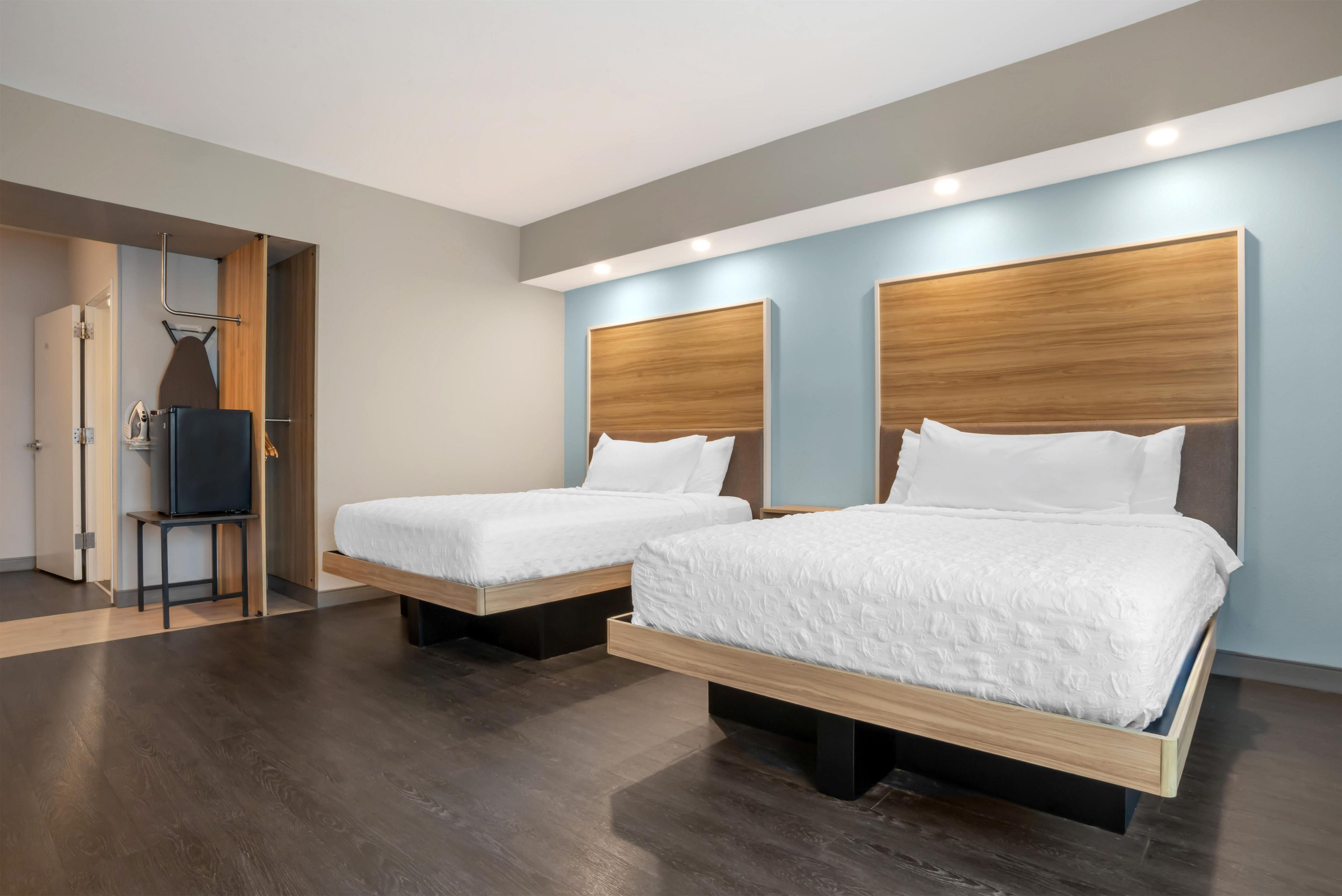 Habitación de hotel con dos camas, cabecera de madera, televisor de pantalla plana y vestidor.