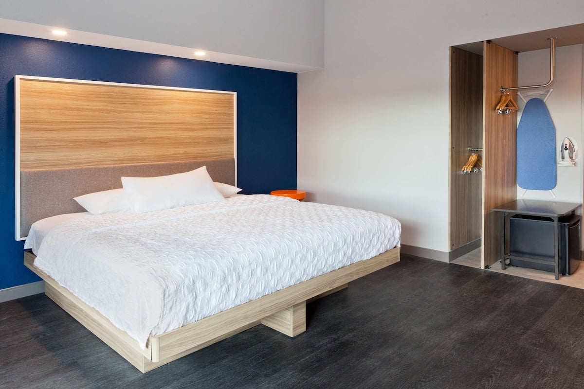 A modern bedroom with a large bed, a wooden headboard, and a built-in shower area with a mirror and towel rack.