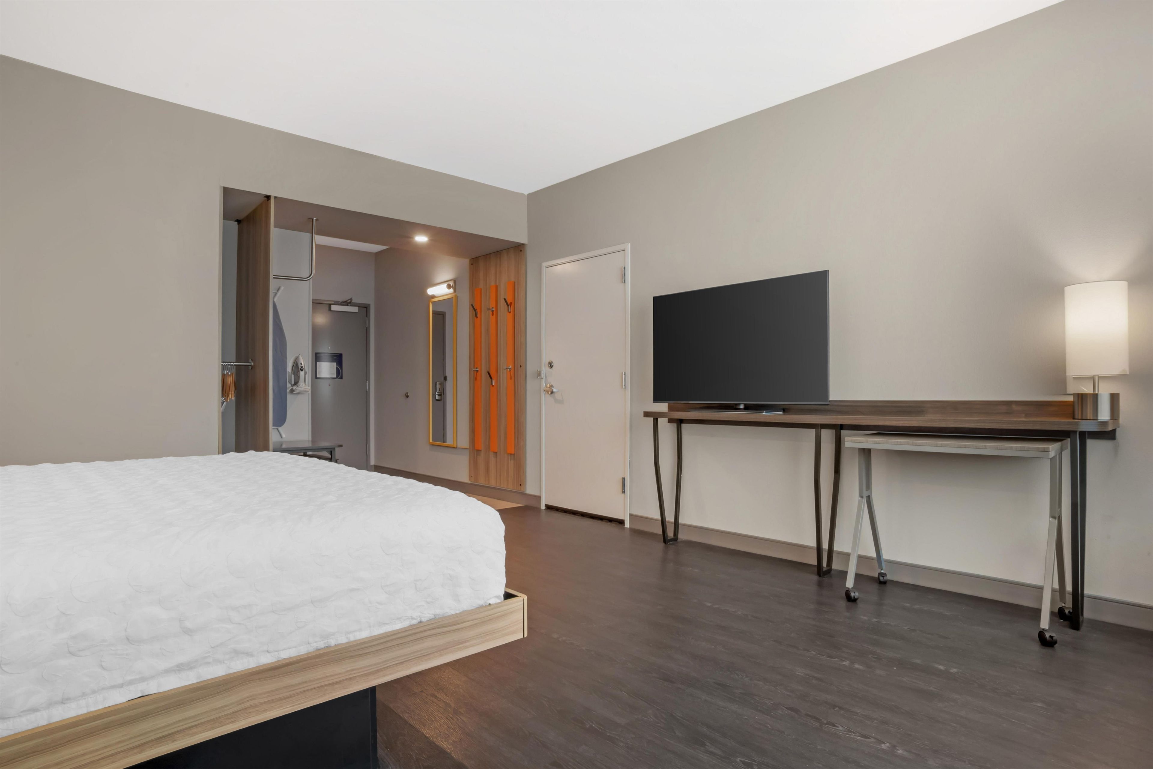 A modern hotel room with a bed, a flat-screen TV, a desk with a lamp, and a shower area.