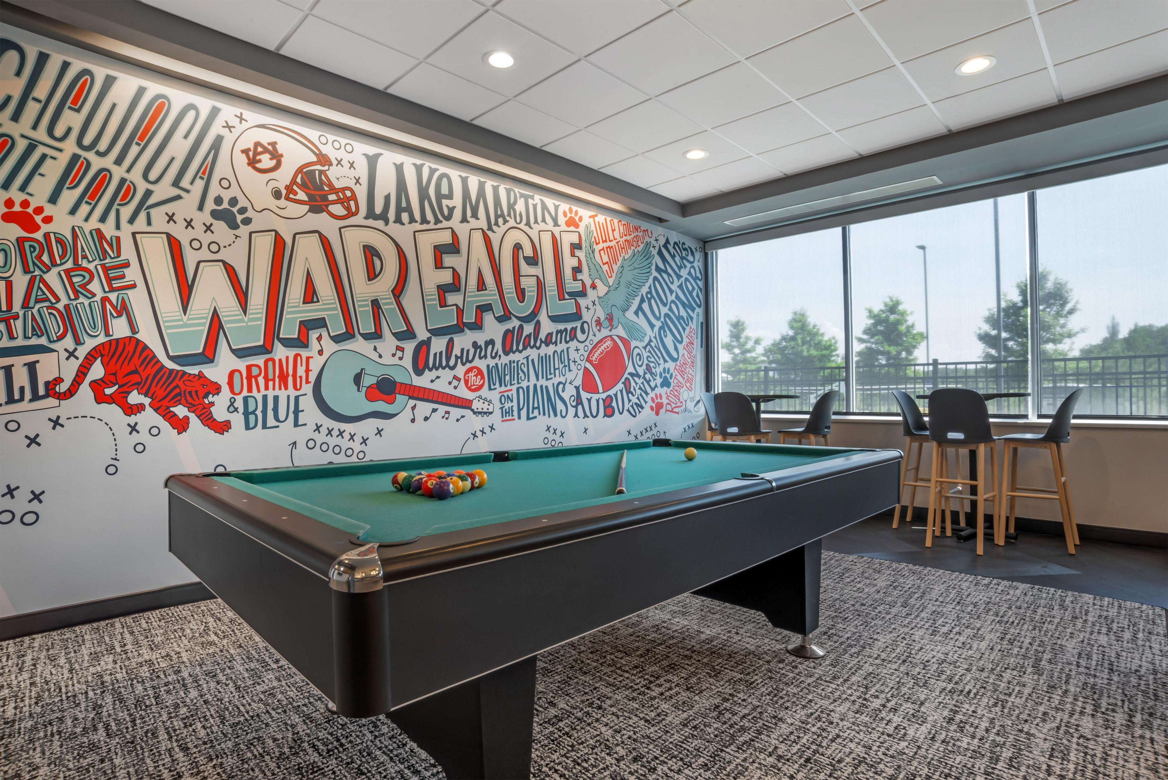 Een pooltafel in een ruimte met een muurschildering met sport- en muziekthema's, een raam met uitzicht en moderne meubels.