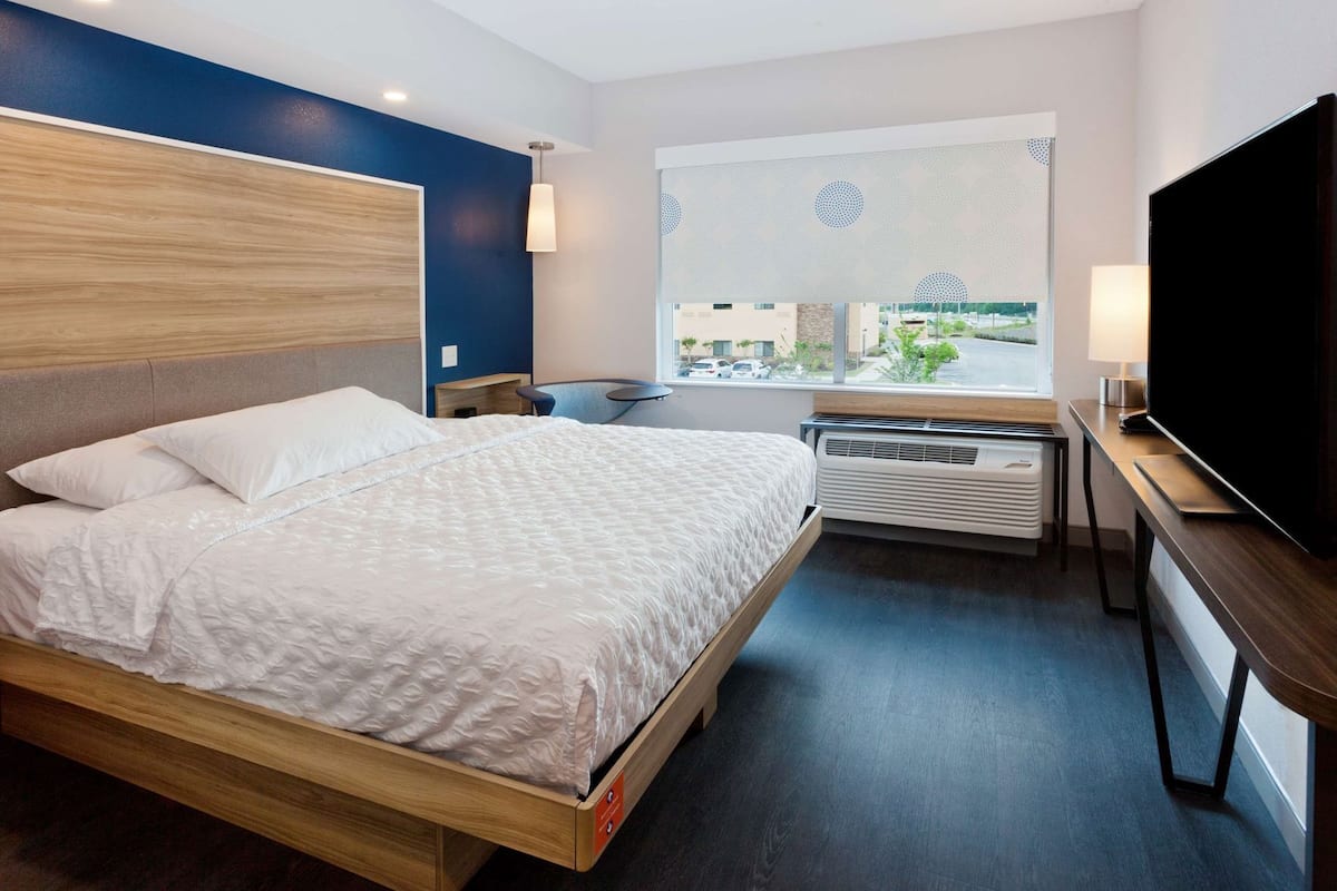 A hotel room with a bed, a TV, a window with a view, and a heater.