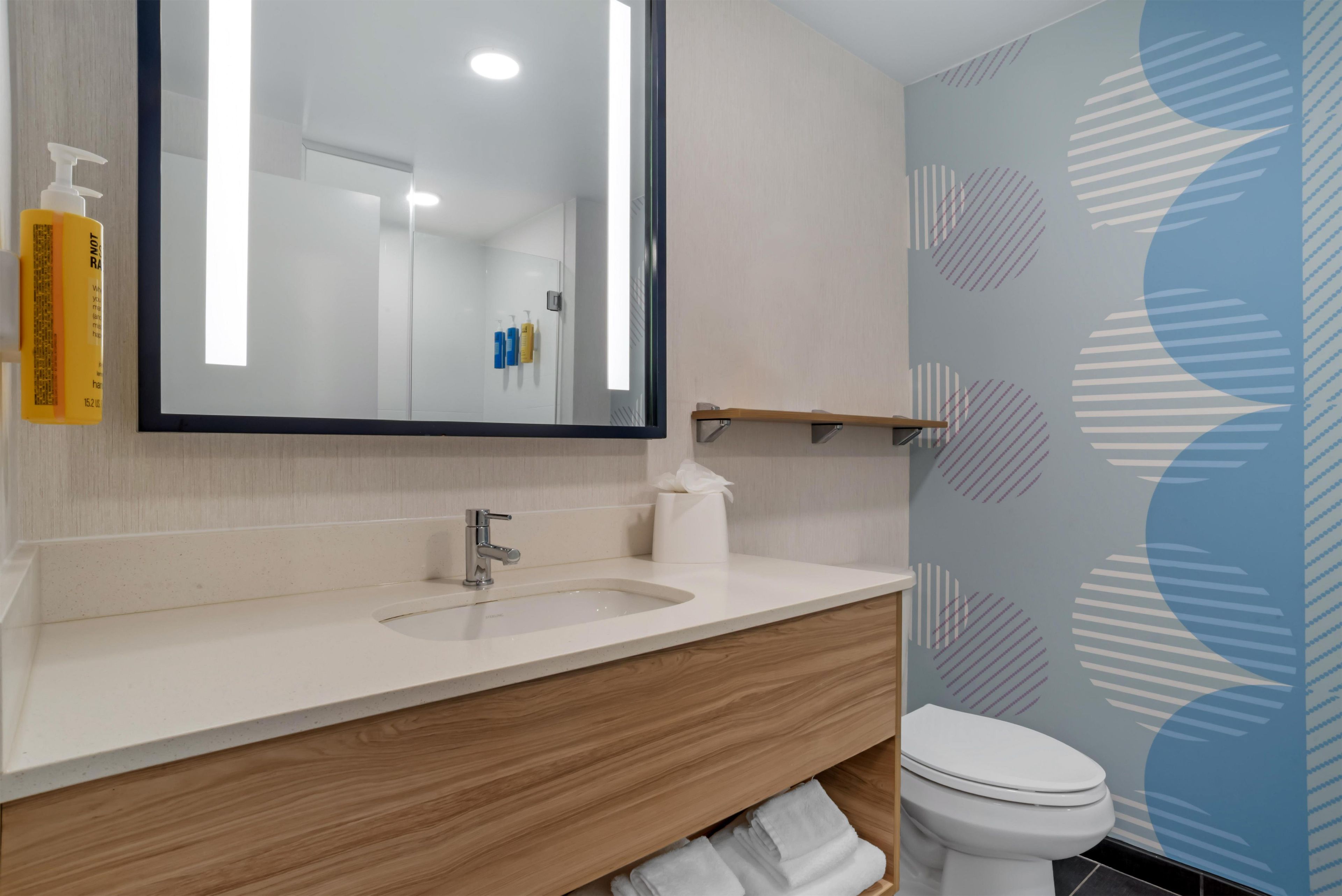 A modern bathroom with a large mirror, a sink, a toilet, and a towel rack.