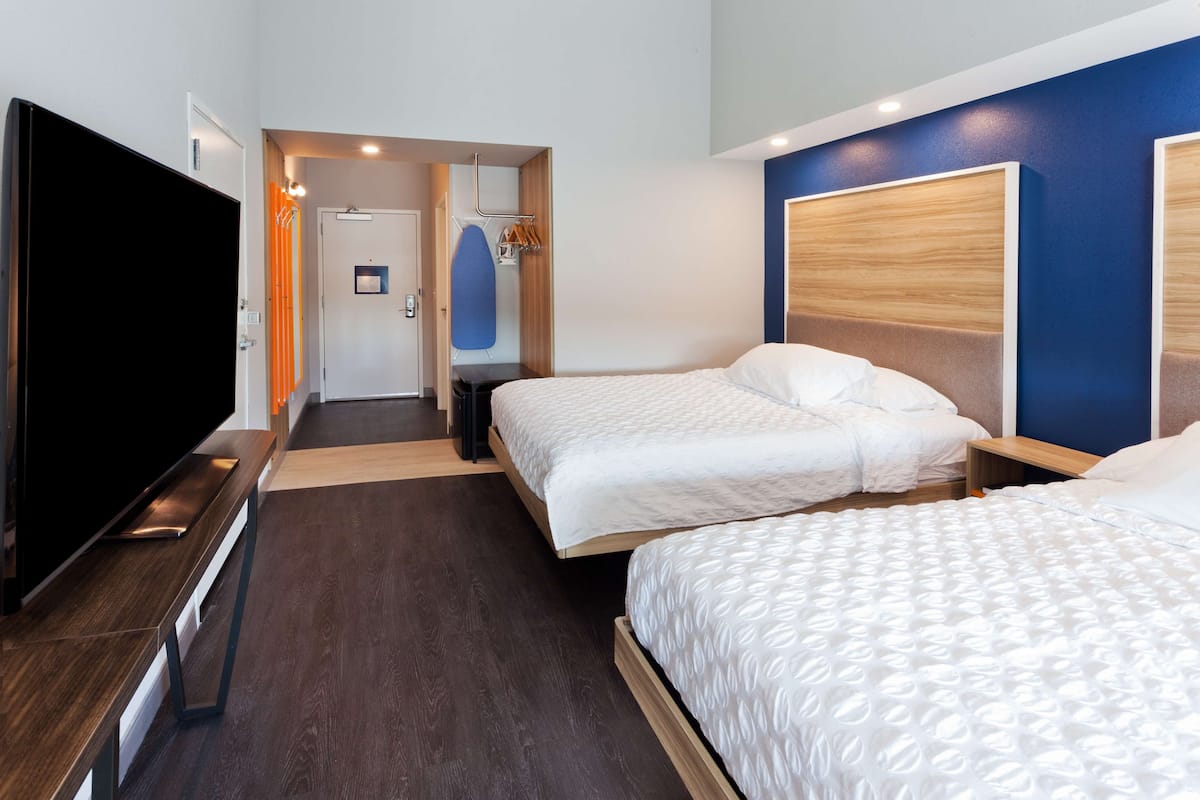 A hotel room with two beds, a TV, a desk, and a bathroom visible through an open door.