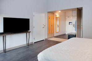 A modern hotel room with a large bed, a flat-screen TV on a stand, a wooden door with a mirror, and a shower area.