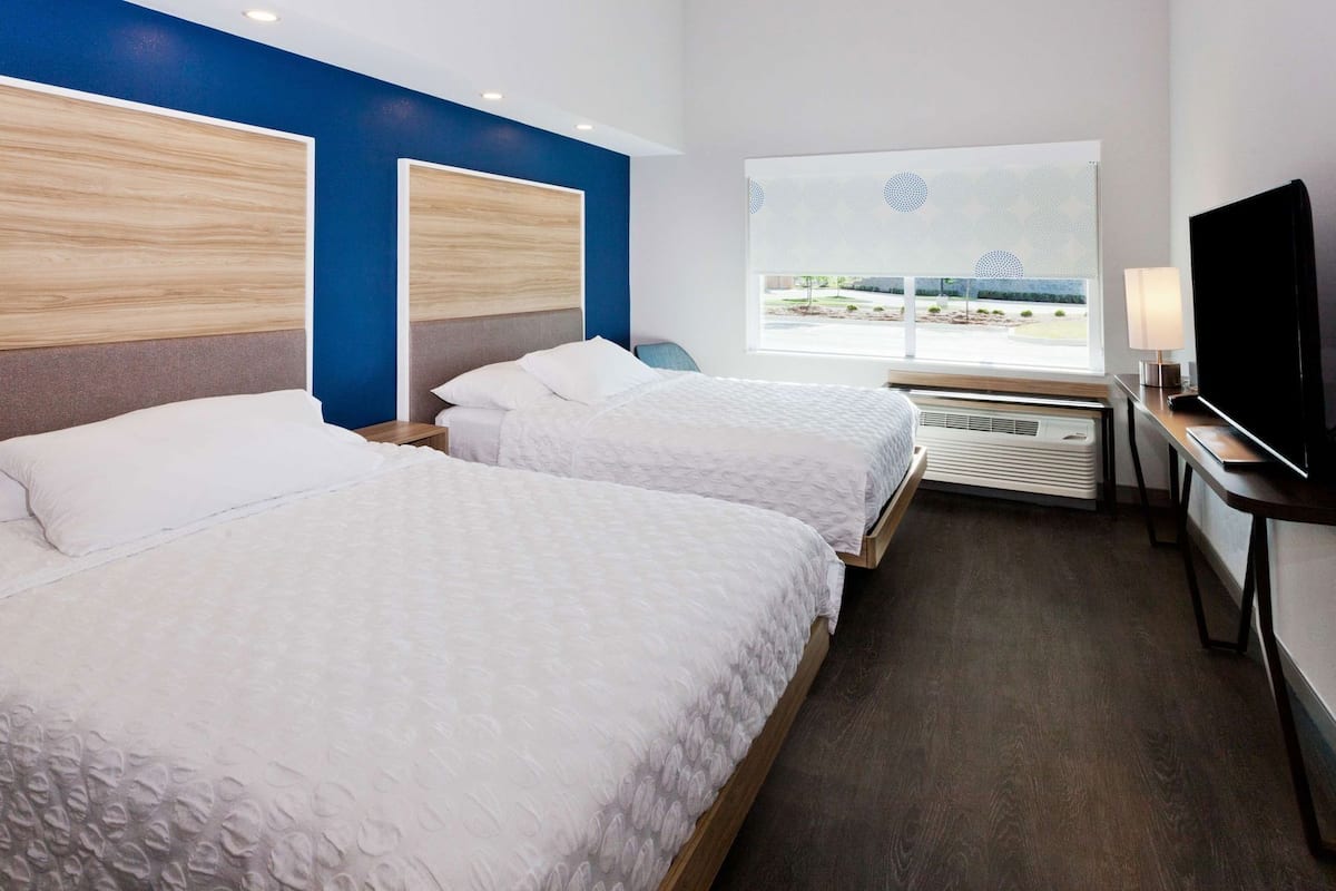 A hotel room with two beds, a TV, a desk, and a window with a view of a park.