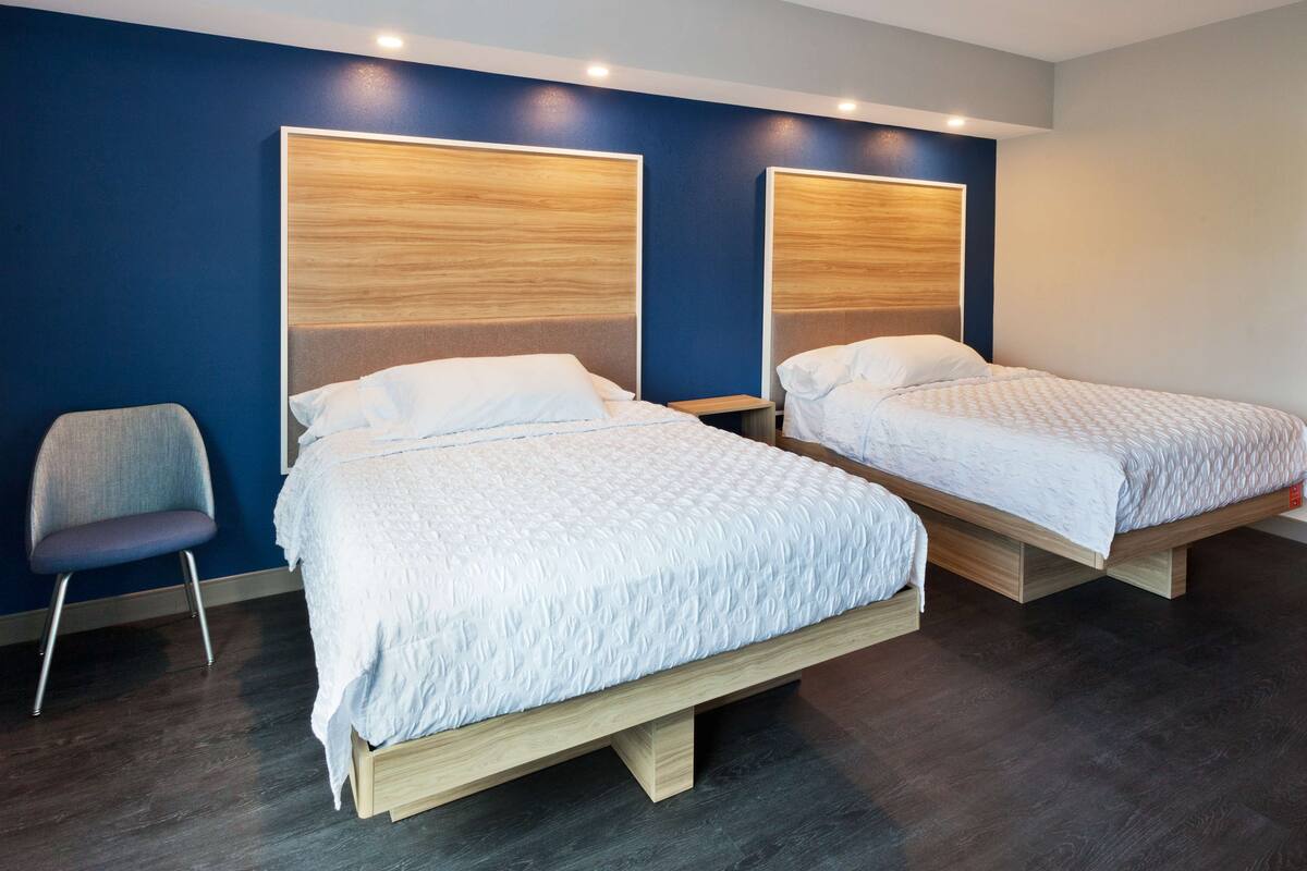 A modern hotel room with two single beds, a chair, and a dark wooden floor.