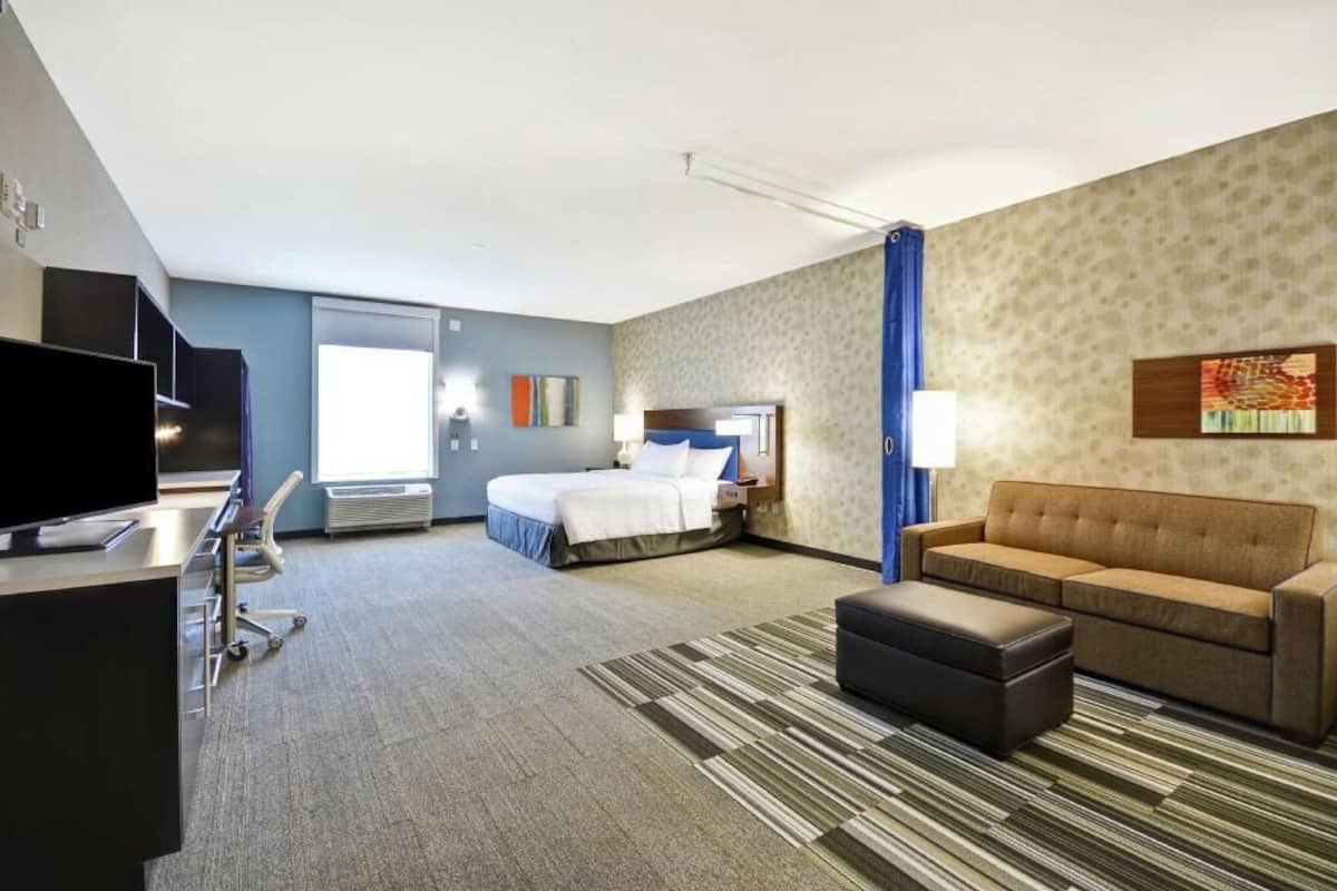 A hotel room with a bed, a sofa, a TV, a desk, and a window.