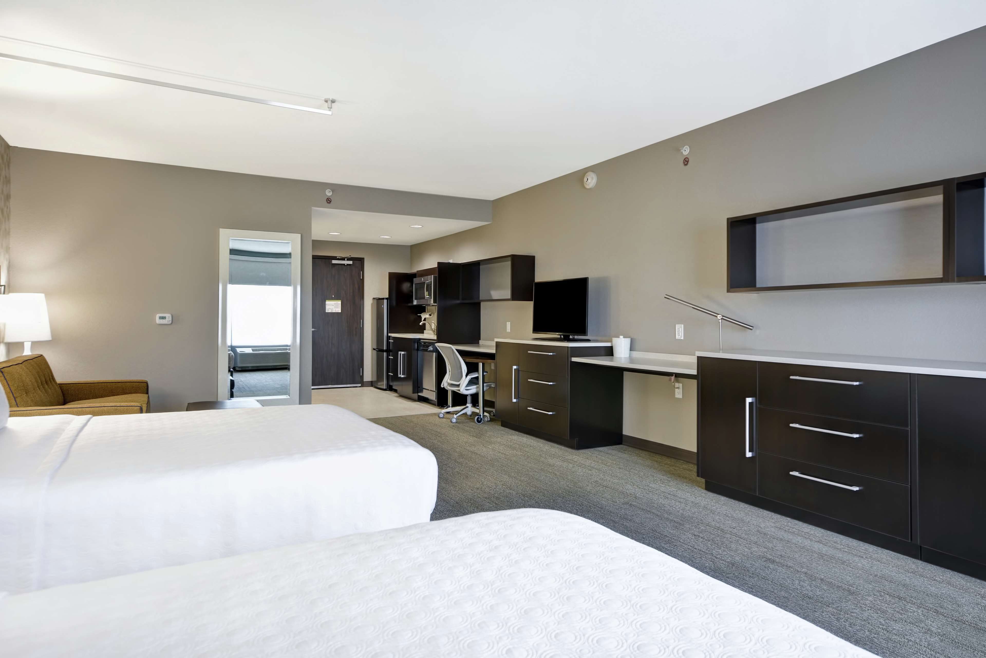 A hotel room with two beds, a desk, a chair, and a kitchenette.