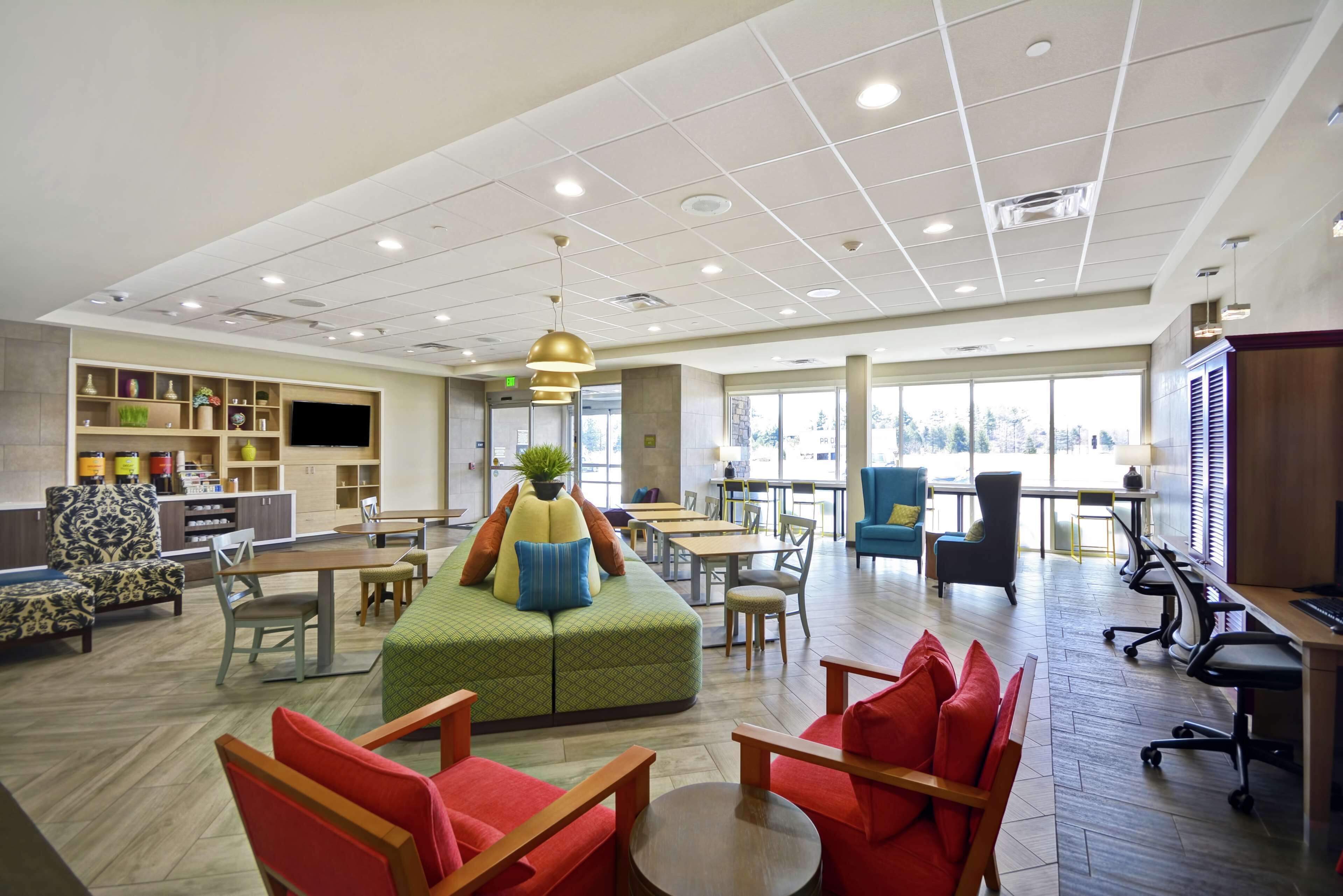 A spacious lobby with a green sofa, red chairs, a kitchen area, and a large window providing natural light.