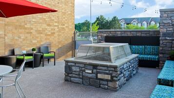 An outdoor patio with stone seating, a grill, and string lights.