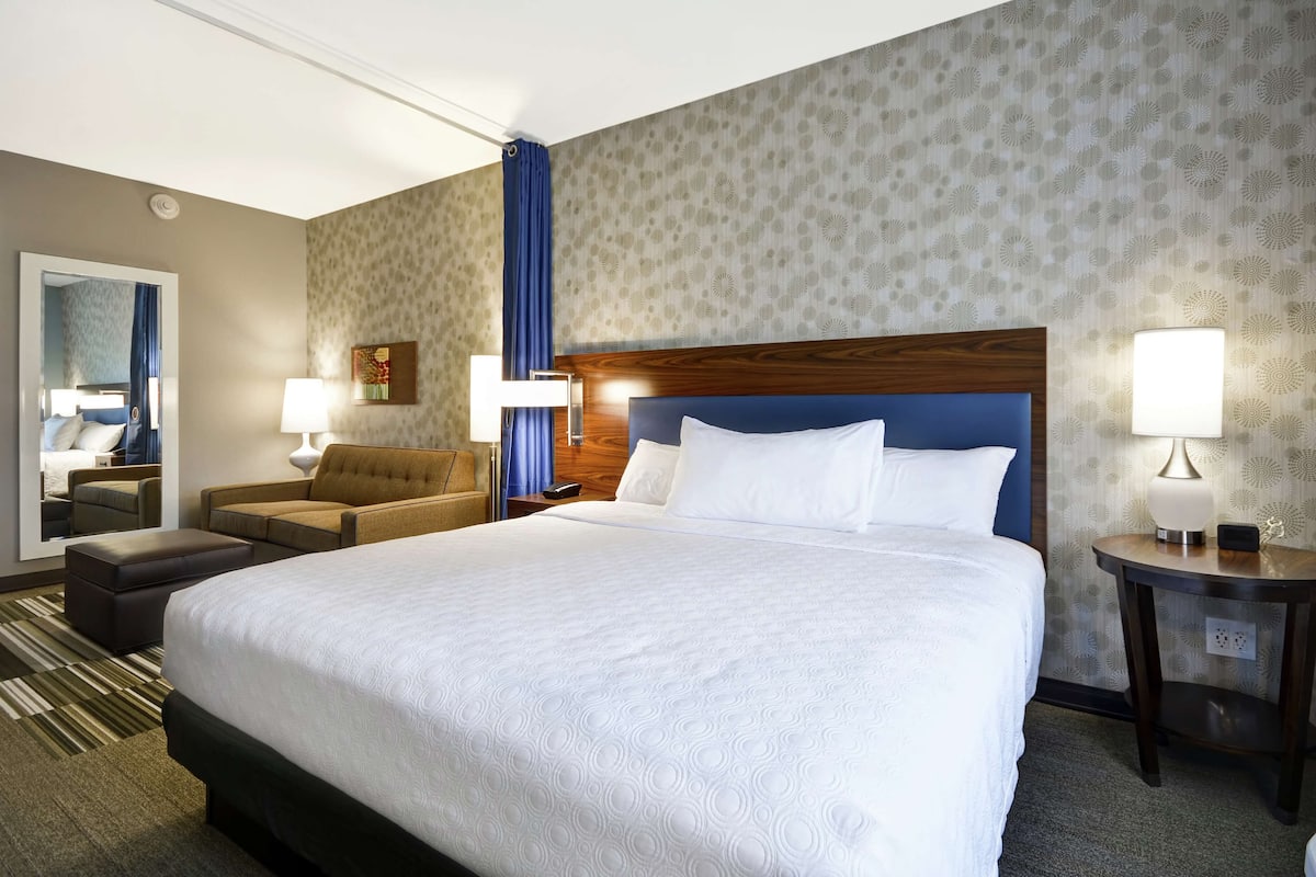 A hotel room with a large bed, a sofa, a desk, and a mirror.