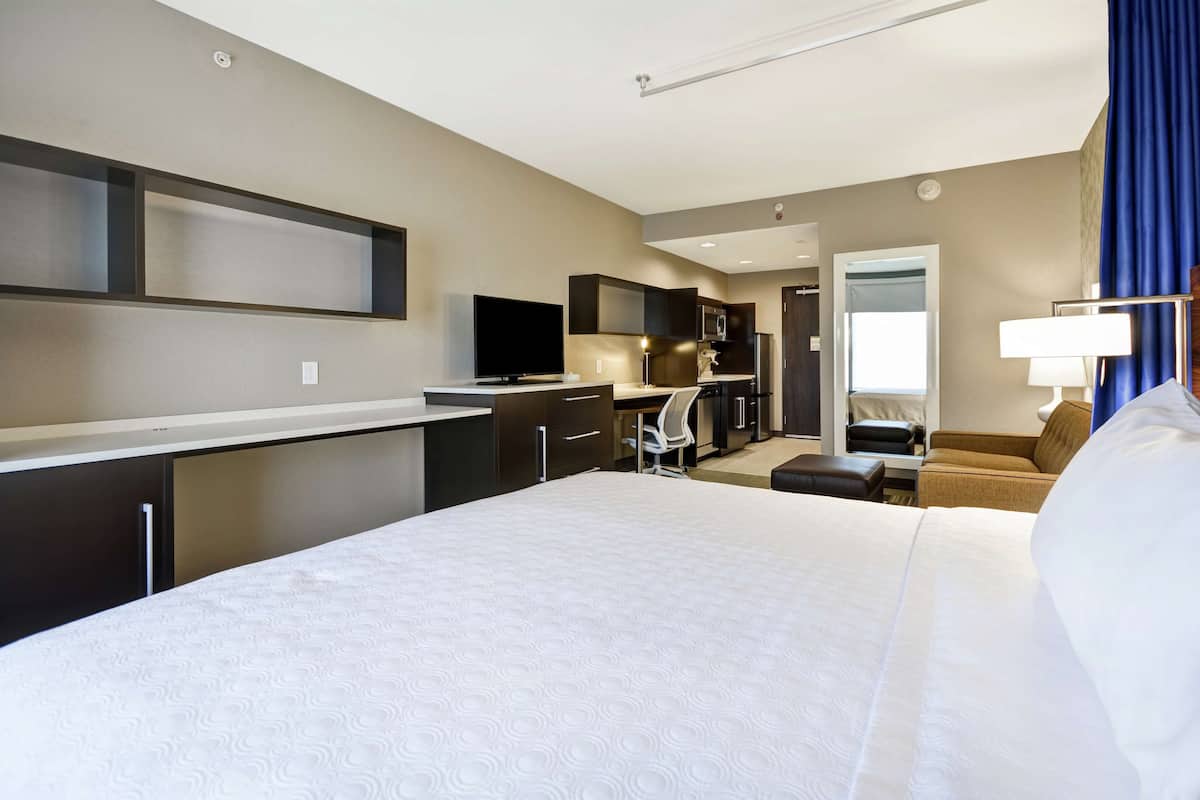 A hotel room with a large bed, a desk, a television, a kitchenette, and a bathroom.