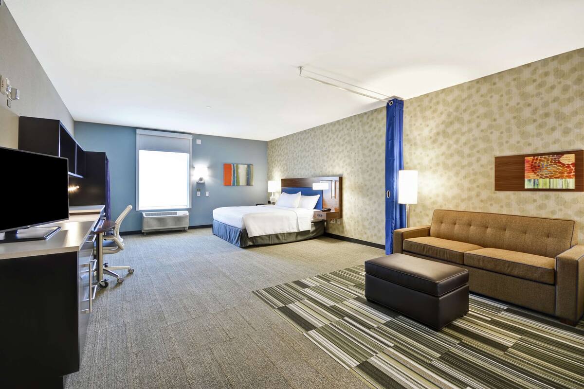 A hotel room with a bed, a sofa, a TV, a desk, and a window.