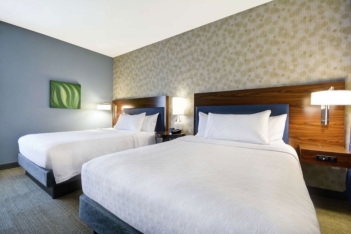 A hotel room with two beds, a nightstand with a lamp, and a wall-mounted artwork.