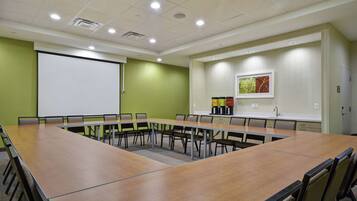 A conference room with a long table, chairs, a projector screen, and a coffee station.