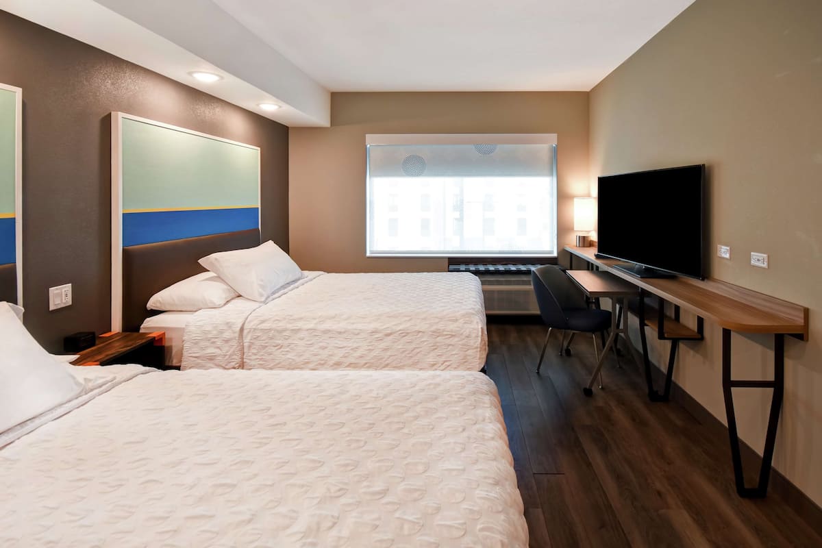 Une chambre d’hôtel avec deux lits, un bureau, une télévision et une fenêtre avec des stores.
